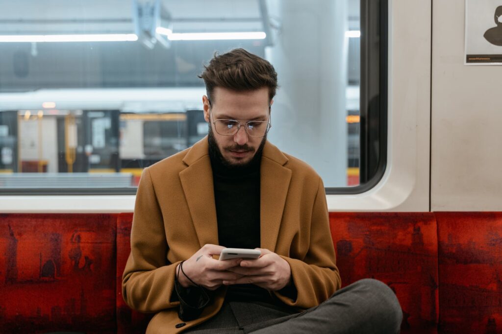 man in brown coat sitting on red seat while texting